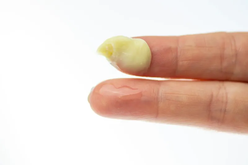 Close-up of natural skincare balm texture on fingertip against white background