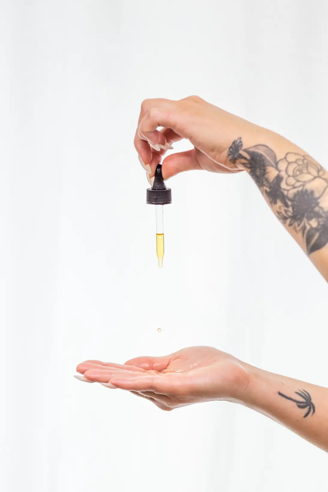 Lifestyle photography of tattooed hands using a golden skincare oil dropper