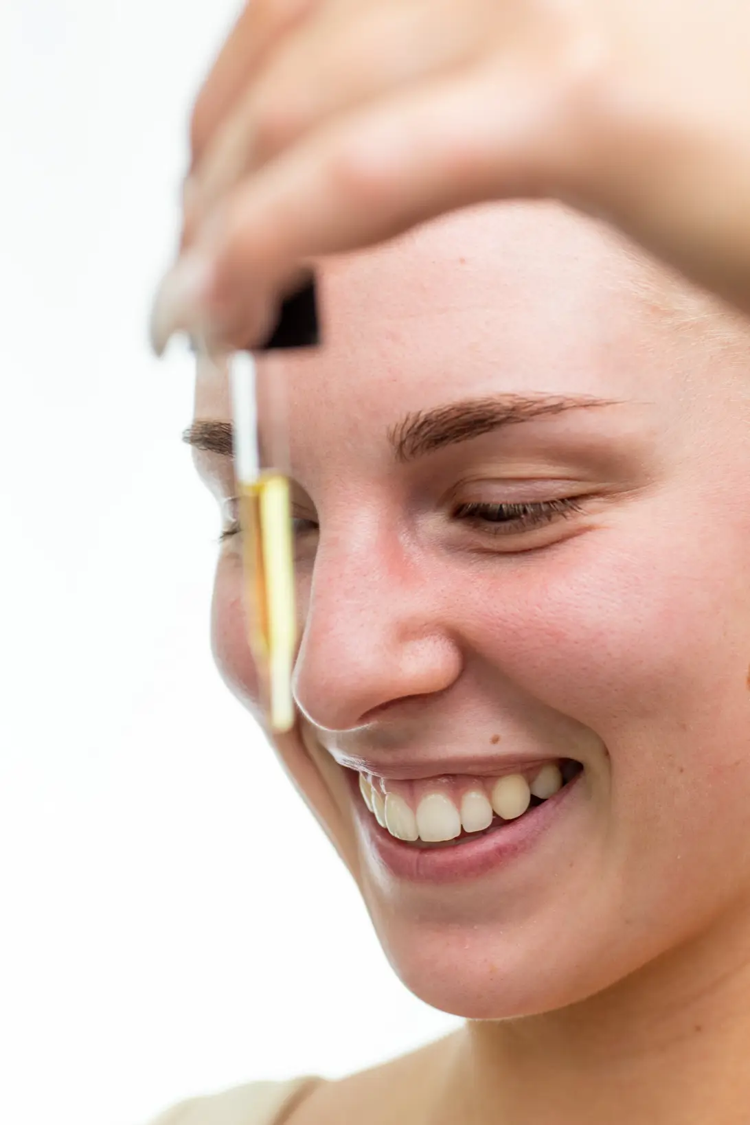 Close-up portrait of smiling woman applying skincare serum with dropper