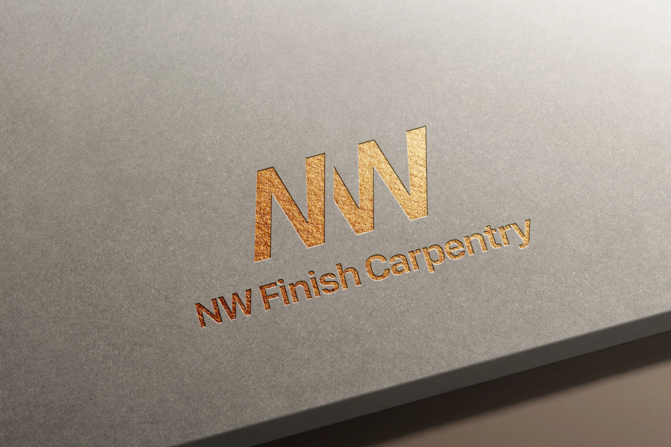 Gold foil embossed NW Finish Carpentry logo on smooth gray cardstock, showing the stylized NW monogram with saw blade-inspired angular letterforms above the company name in elegant metallic serif typography