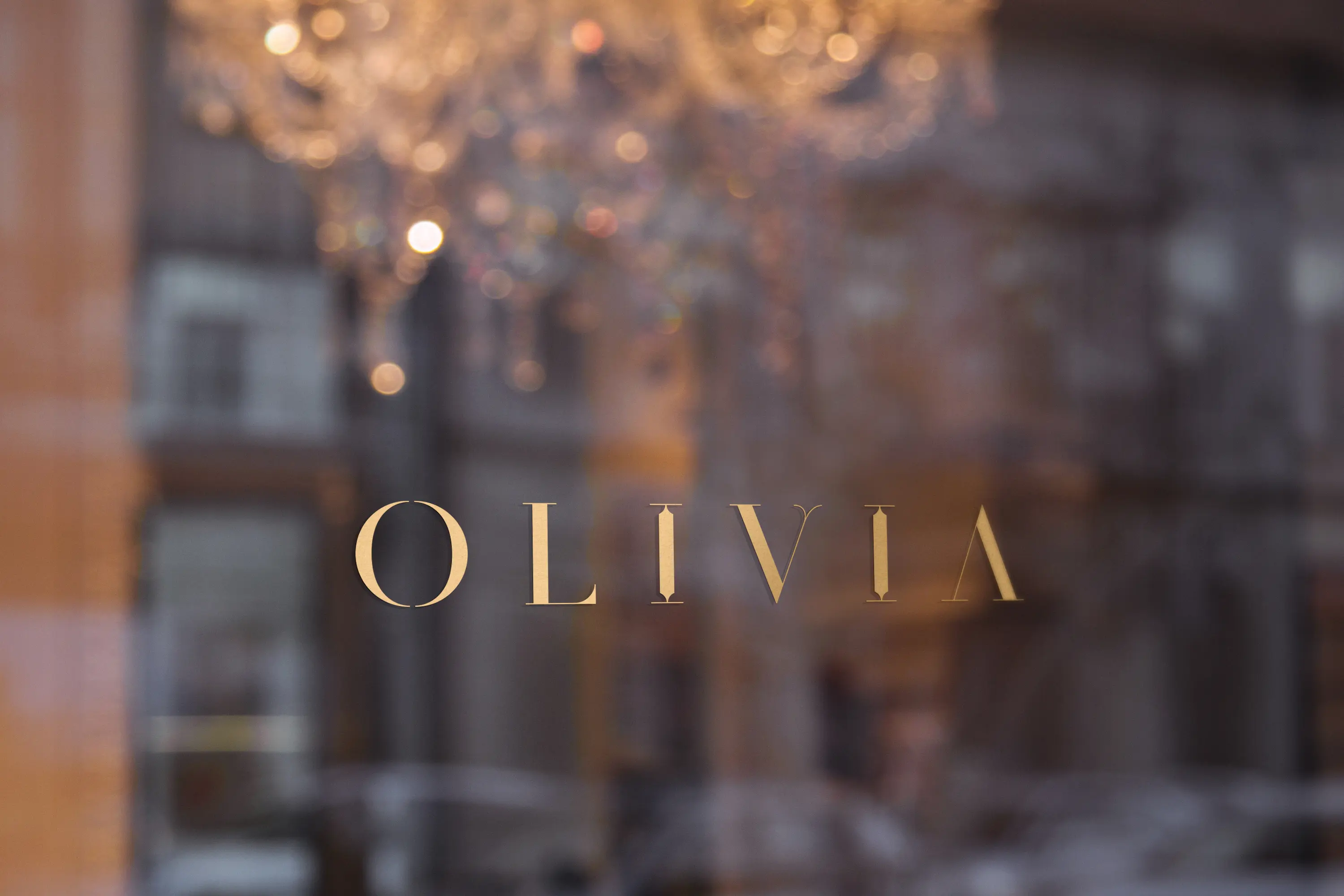 Olivia wordmark in gold on storefront glass with crystal chandelier visible through the window in Bilbao Casco Viejo